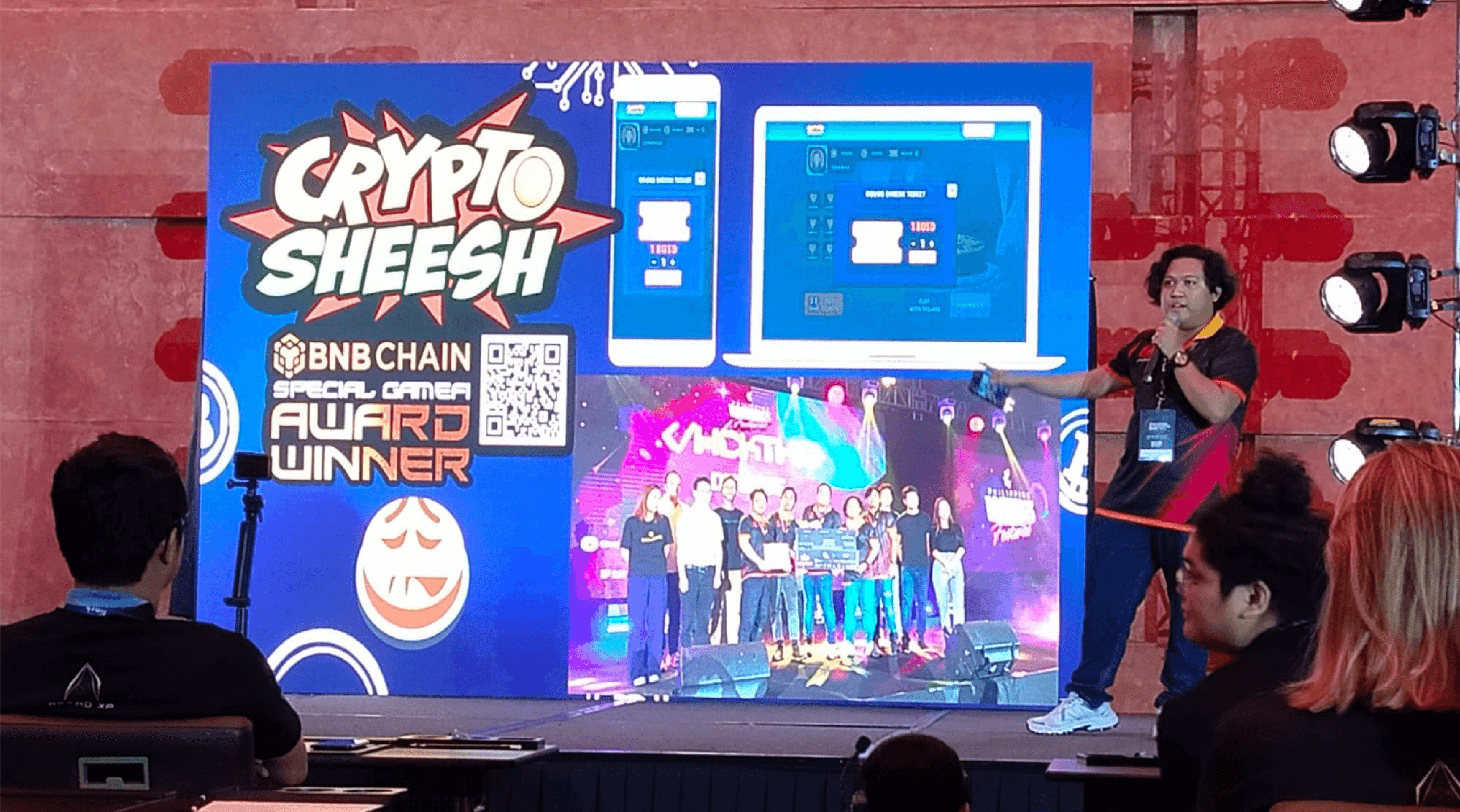 A DvCode speaker presenting on stage beside a large screen showing the Crypto Sheesh project and its BNB Chain special gamer award.